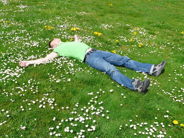 Moški se sprošča tako, da leži na travi.