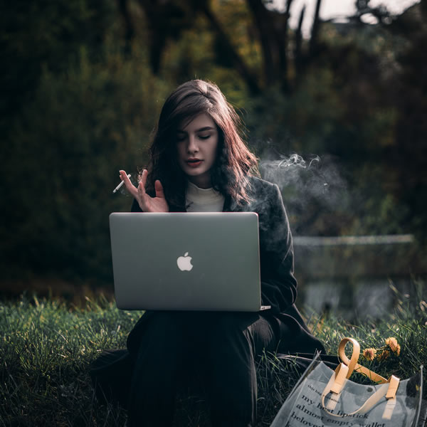 Slika prikazuje dekle, ki kadi in dela za računalnikom.