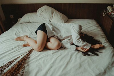 Na sliki je dekle, ki zaradi bolečin leži na postelji.
